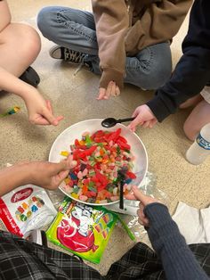 several children are sitting on the floor with their hands in a bowl full of candy