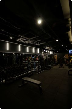 a dimly lit gym with rows of dumbbells and benches in the foreground