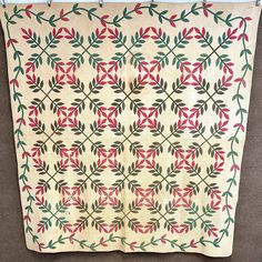 an old quilt hanging on a wall next to a brown floor with a red and green flowered design