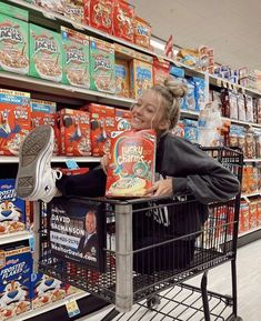 a woman pushing a shopping cart through a store filled with food and snacks on shelves