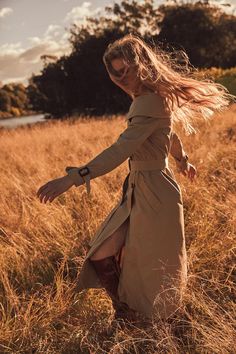 a woman in a trench coat walking through tall grass