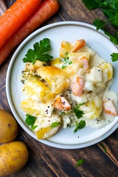 a white plate topped with food next to two carrots and potatoes on top of a wooden table