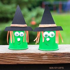 two green plastic cups with googly eyes and witches hats on them sitting on a wooden table