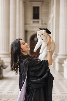 a woman holding up a cat in front of an old building with columns and pillars