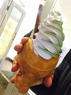 a person holding an ice cream cone with green and white icing on it's top