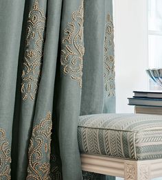 a close up of a chair with curtains in front of it and books on the table