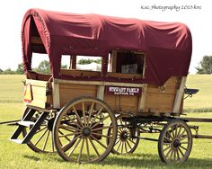 an old fashioned wagon with a red tarp on it's top is parked in the grass