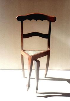 a wooden chair sitting on top of a white floor next to a wall with a shadow cast on it