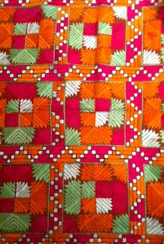 an orange and red quilt with green leaves on it