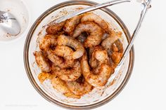 a bowl filled with cooked shrimp next to a spoon and sauce on a white table