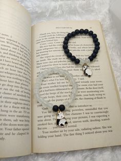 an open book with a beaded bracelet on it and a dog charm hanging from the clasp