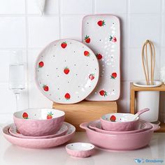 pink and white dishes with strawberries on them are sitting on a counter next to utensils