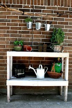 a shelf with plants and watering can on it in front of a brick wall,