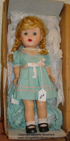 an old doll in a box with tags on it's collar and legs, wearing a blue dress