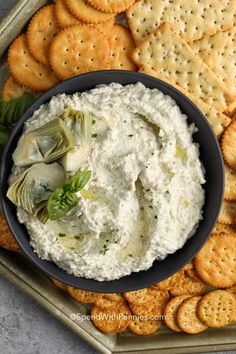 hummus and artichoke dip in a bowl surrounded by crackers