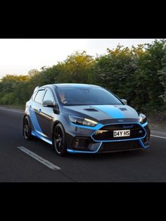 a blue and black car driving down the road with trees in the backgroud