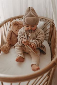 a baby sitting in a crib with a teddy bear