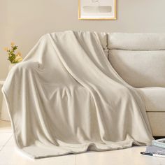 a white couch covered in a blanket next to a coffee table with flowers on it