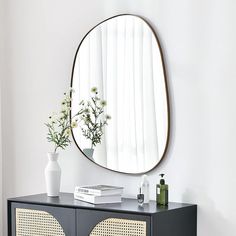 a round mirror on the wall above a black cabinet and vase with flowers in it