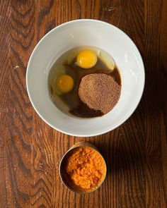 three eggs and spices in a white bowl on a wooden table next to a measuring cup