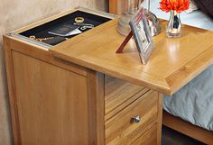 a bed with a wooden night stand on top of it next to a vase filled with flowers