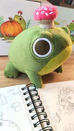 a green frog with a mushroom on its head sitting next to a notebook and pencil