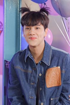 a young man wearing a denim shirt and tie with balloons in the background at a birthday party