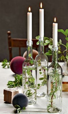 three bottles filled with plants sitting on top of a table next to candles and other items