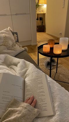 a person laying in bed reading a book with two candles on the end table next to them