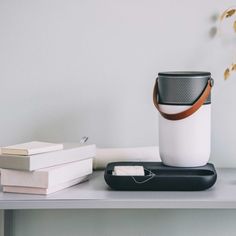 a white and black speaker sitting on top of a table next to books, a vase with flowers