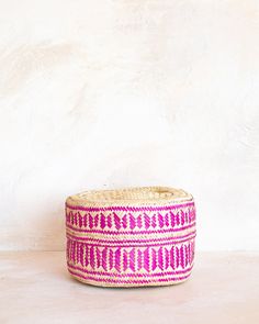 a pink and white woven basket sitting on top of a wooden table next to a wall