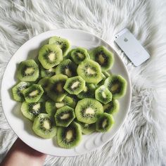 a white plate topped with sliced kiwis on top of a furry rug next to an ipod