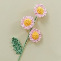 three crocheted flowers with leaves on top of a white surface, one is pink and the other is green