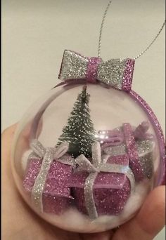 a hand holding a glass ornament with a christmas tree and presents in it