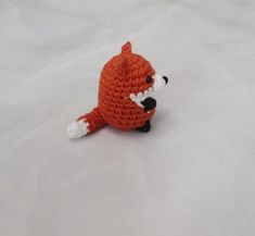 a small crocheted stuffed animal sitting on top of snow covered ground with it's mouth open