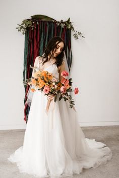 a woman in a wedding dress holding a bouquet with flowers on the floor next to a wall