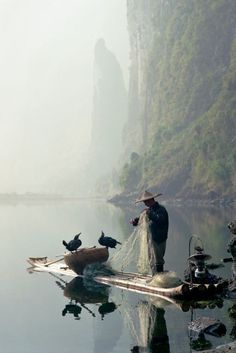 a man standing on top of a boat filled with lots of water next to mountains