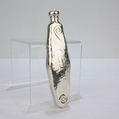 a silver vase sitting on top of a clear table next to a glass box filled with liquid