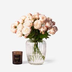 a glass vase filled with white roses next to a jar of wax and a candle