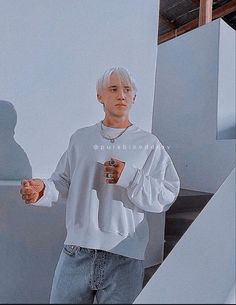 a man with white hair is standing in front of stairs and holding a coffee cup