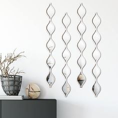 three metal wall sculptures hanging on a white wall next to a black cabinet and potted plant