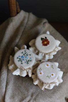 three embroidered flowers are sitting on top of a piece of cloth, next to a wooden chair