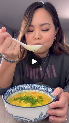 a woman eating soup from a blue and white bowl with a spoon in her mouth