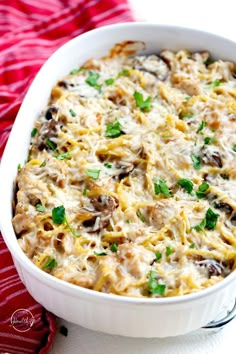 a white casserole dish filled with pasta and mushrooms, garnished with parsley