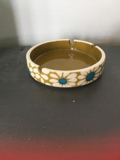 a yellow and white flowered bowl on a black table with water in the middle