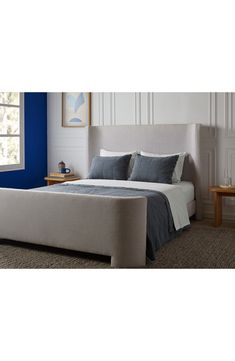 a bed with blue and white sheets in a room next to a window on carpeted floor