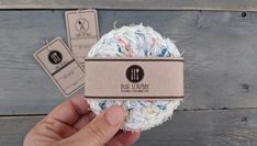 a ball of yarn is being held in front of a wooden background with two tags