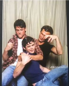 three young men sitting on top of each other in front of a white curtain with one pointing at the camera