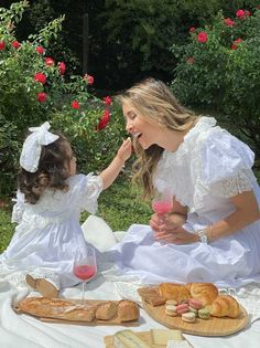 a mother and daughter sitting at a table with bread, wine and pastries on it