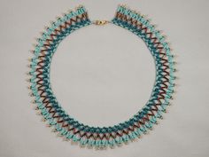 a blue and brown beaded necklace on a white surface with gold beads in the shape of trianglees